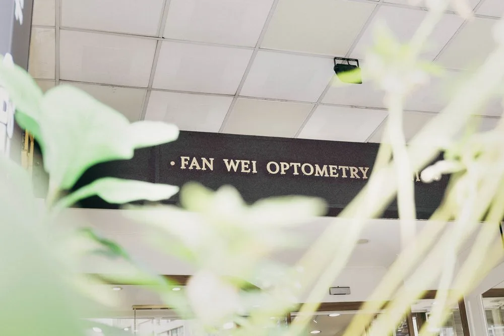 綠色植栽間望向 FAN WEI OPTOMETRY 黑底金字招牌