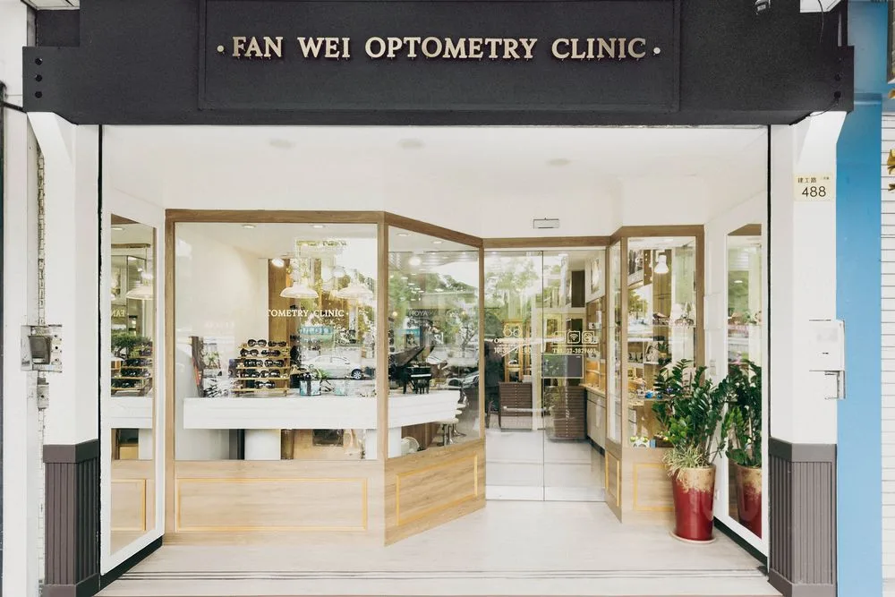 峰瑋眼鏡店面外觀:黑底金字 FAN WEI OPTOMETRY CLINIC 招牌與木質窗框玻璃櫥窗