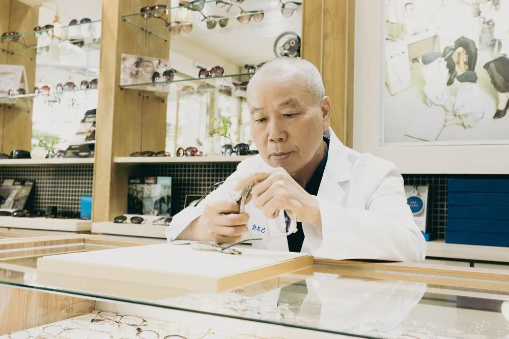 資深白袍職人在玻璃櫃檯前檢視手中的眼鏡