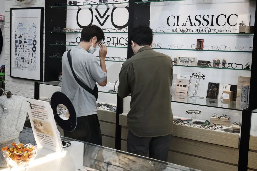兩位顧客在 OVVO OPTICS 與 CLASSICO 品牌牆前試戴鏡框