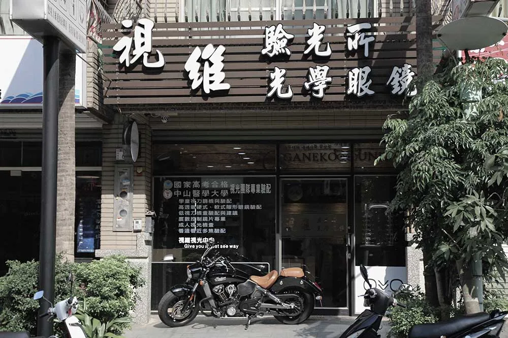 視維驗光所光學眼鏡店面外觀:木質格柵招牌、玻璃門窗貼與門前停放的重型機車