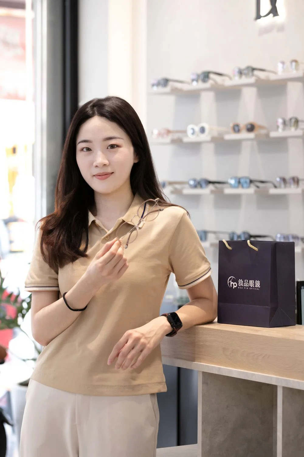 主理人手持鏡框站在櫃檯旁,桌上擺著敘品眼鏡提袋