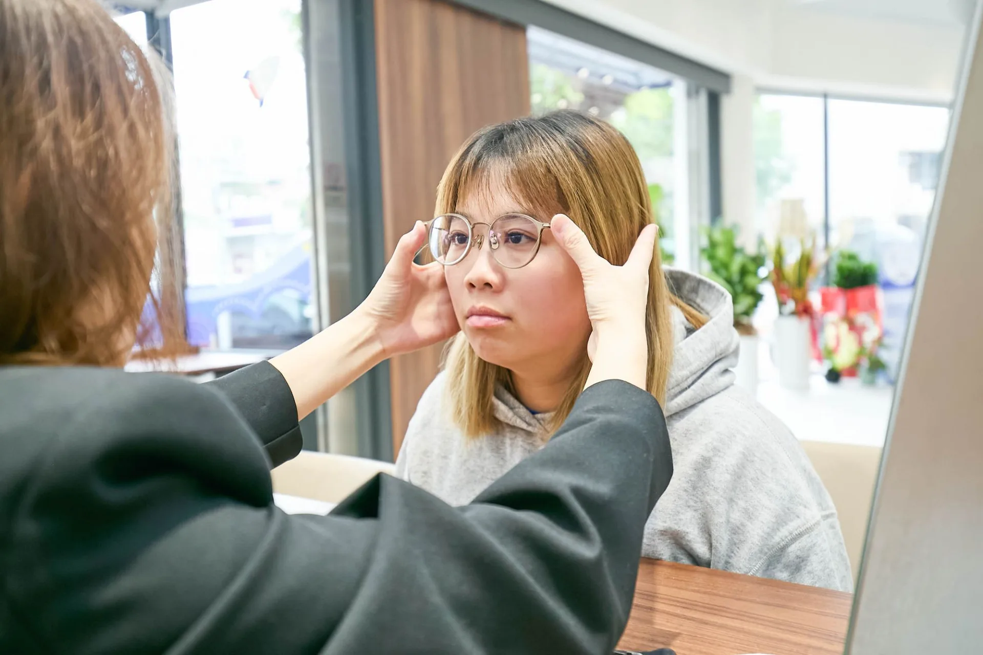門市人員雙手扶著顧客試戴的圓框眼鏡，確認配戴位置