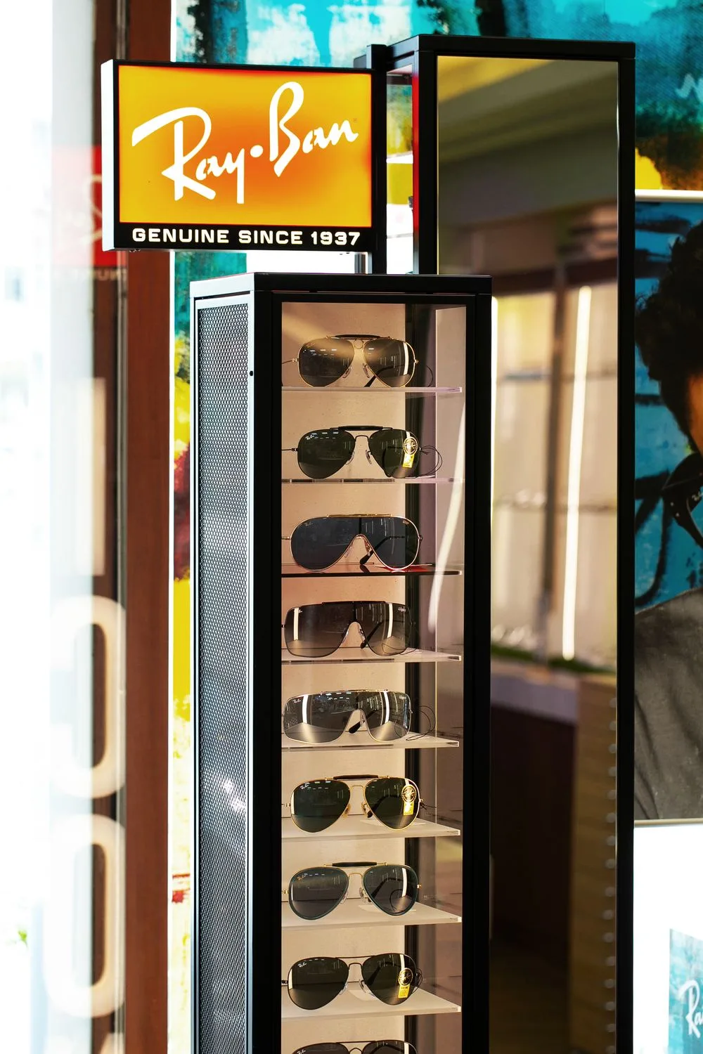 Ray-Ban 直立燈箱陳列櫃:飛行員墨鏡逐層展示,頂端亮著品牌招牌