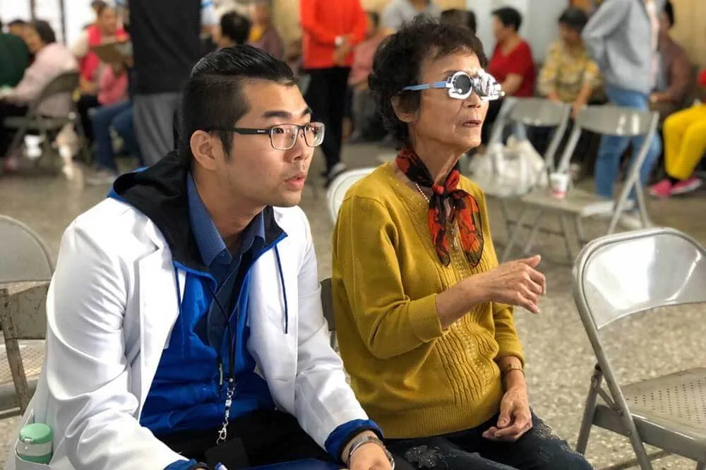 葉育仁老闆在社區公益活動現場,一旁長者配戴試鏡架進行視力檢查