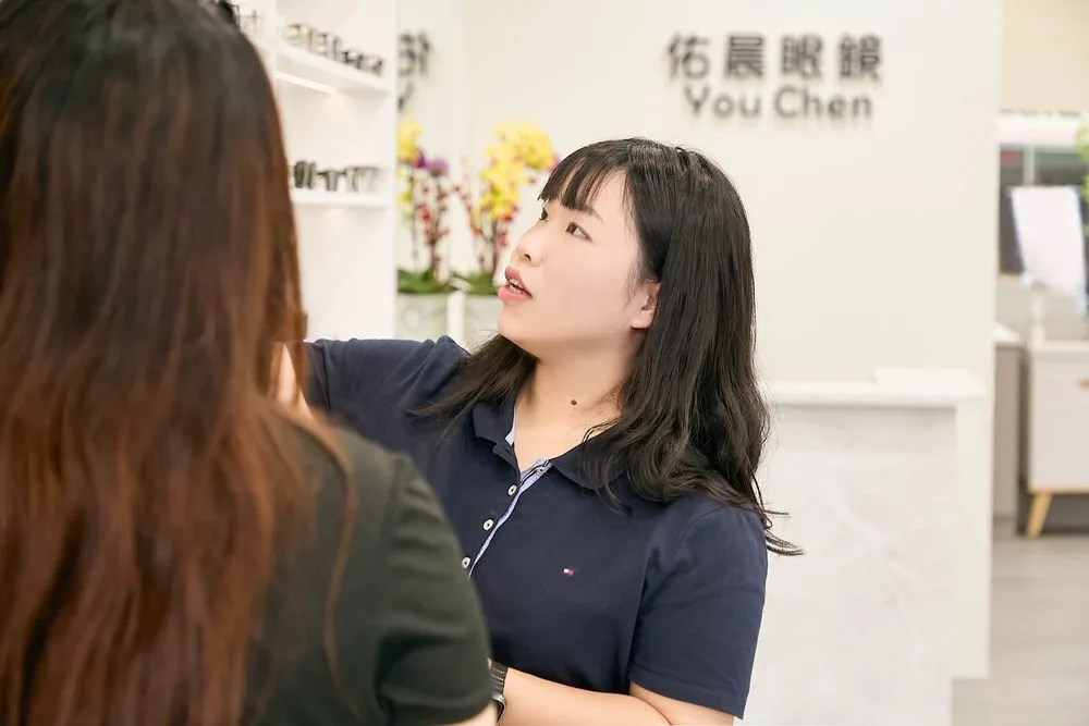 Stella 在佑晨眼鏡標誌牆前與顧客交談