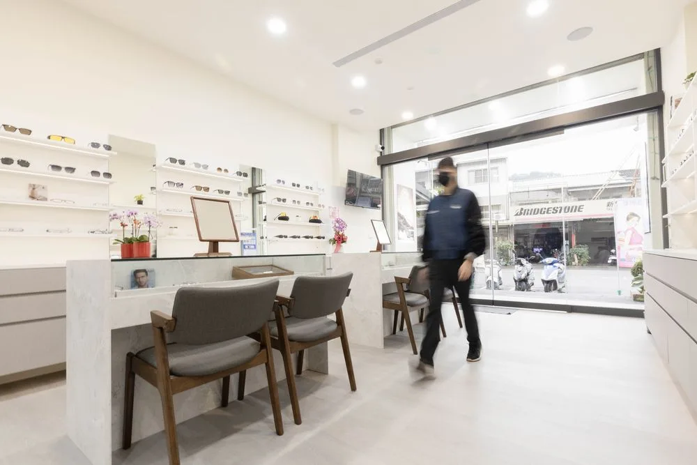 從店內望向玻璃門入口,兩張深灰布面座椅與墨鏡陳列牆