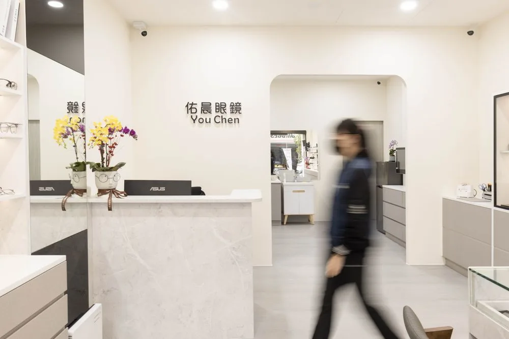 櫃檯區:大理石紋檯面、蘭花盆栽與佑晨眼鏡標誌牆,Stella 走過走道