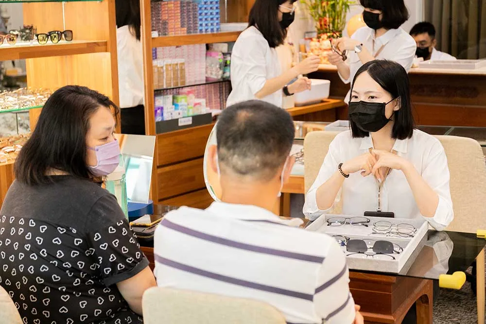 店員在驗配桌前向一對顧客展示鏡框選盤,後方人員各自忙碌