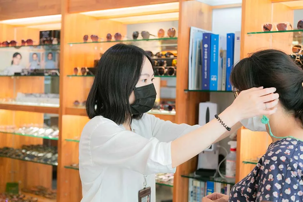 店員為顧客配戴眼鏡並調整位置,身旁是木質層架的墨鏡陳列