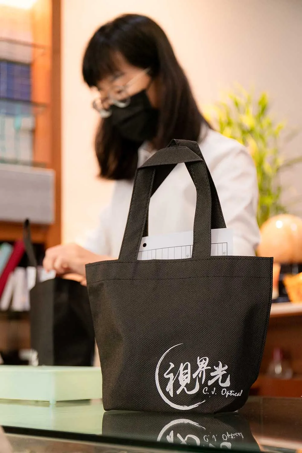 視界光 C.J. Optical 黑色提袋特寫,店員在後方整理物品